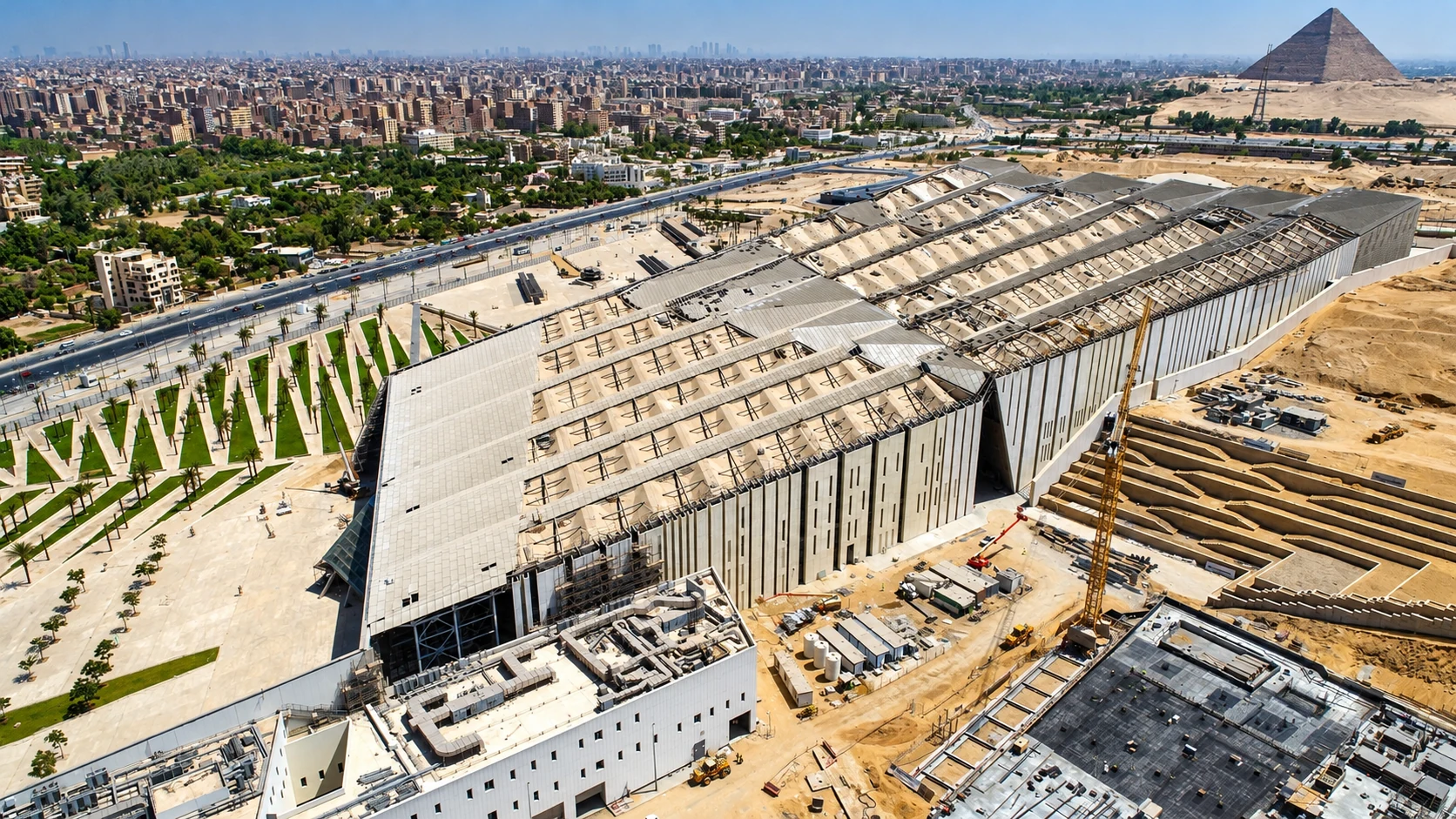 Wide aerial construction view of the Grand Egyptian Museum in Giza with the Great Pyramid beyond